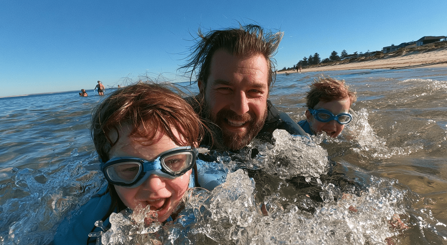 Dad and two kids splashing in the ocean during Australian school holidays